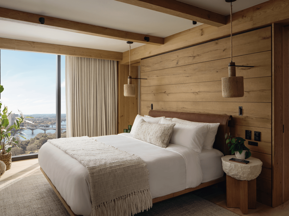 Cama grande num quarto com interior em madeira e uma janela ampla