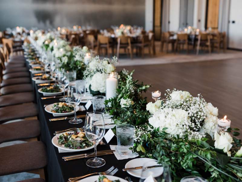 Longue table garnie de grands centres de table fleuris et de salades en assiettes