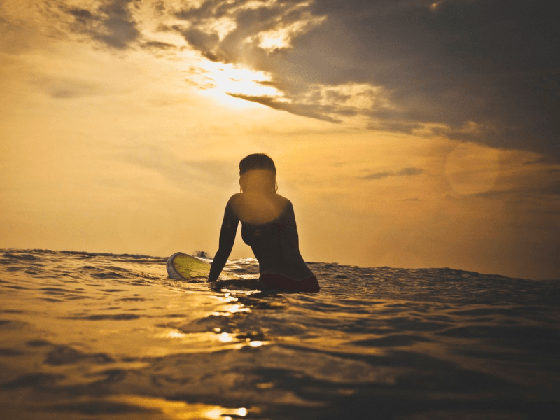 surfer sitting on their board in the water at sunrise