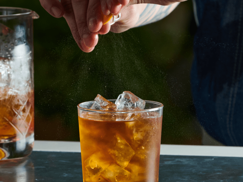 Person spritzing an orange twist over a negroni