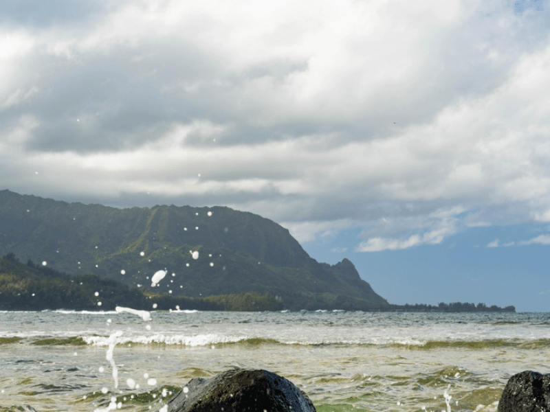 Waves crashing onto rocks with mountains in the background