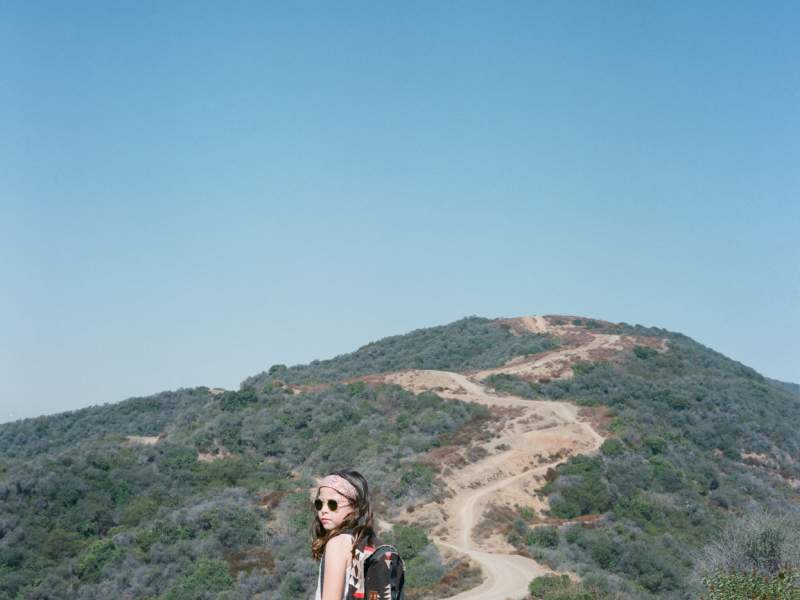 Child wearing a backpack and sunglasses on a hike