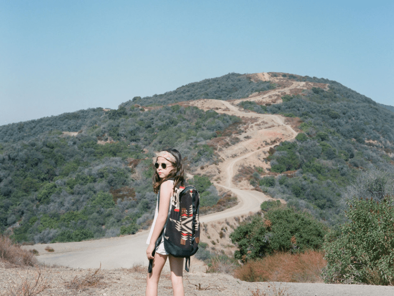 Child wearing a backpack and sunglasses on a hike