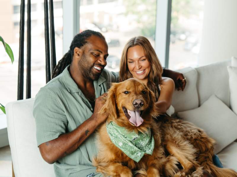 Two people sitting on a couch petting a dog
