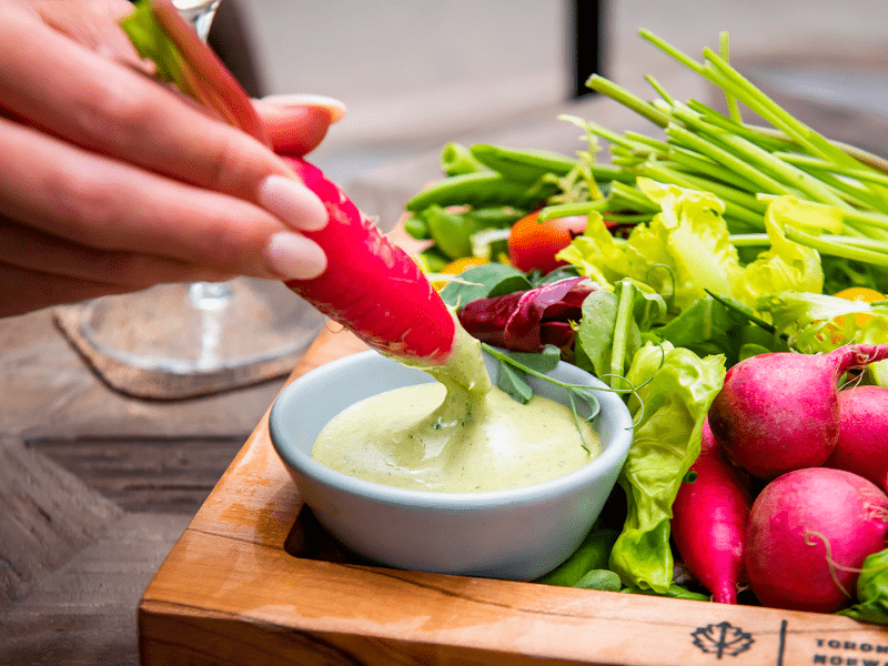 Person dipping a carrot in an avocado dressing