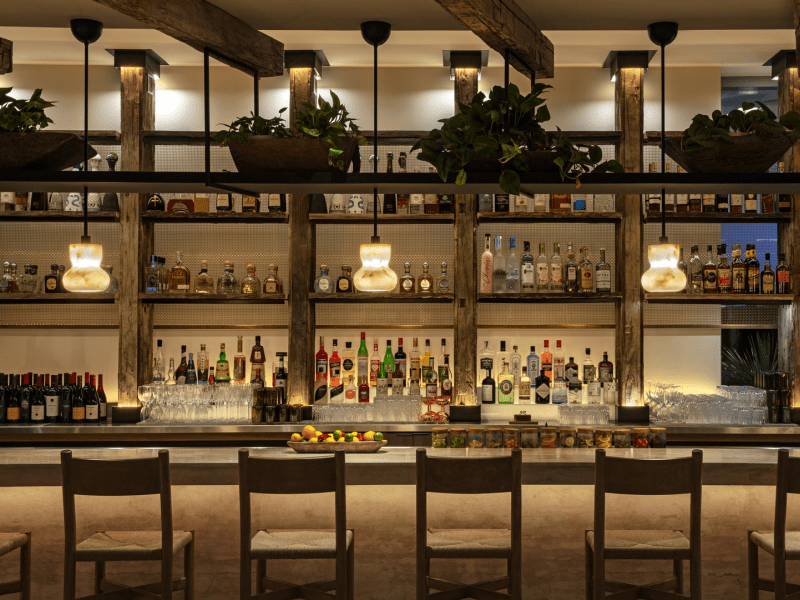 A wide shot view of the bar with ambient lighting hanging from the ceiling over plentiful bar seats