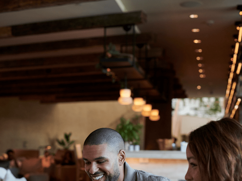 A man and woman laugh while holding their wine glasses in front of them