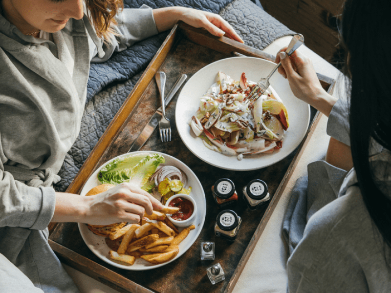 People eating food from a tray in bed