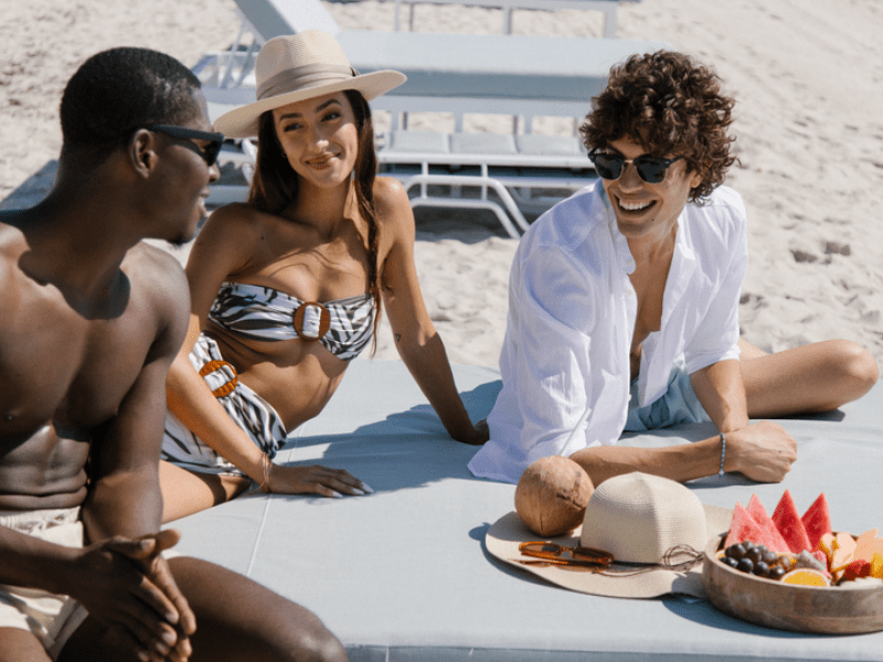 Three people relaxing on a beach chair with some fruit