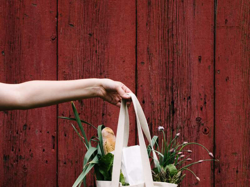 A hand holding a bag full of flowers of bread, in front of a red fence