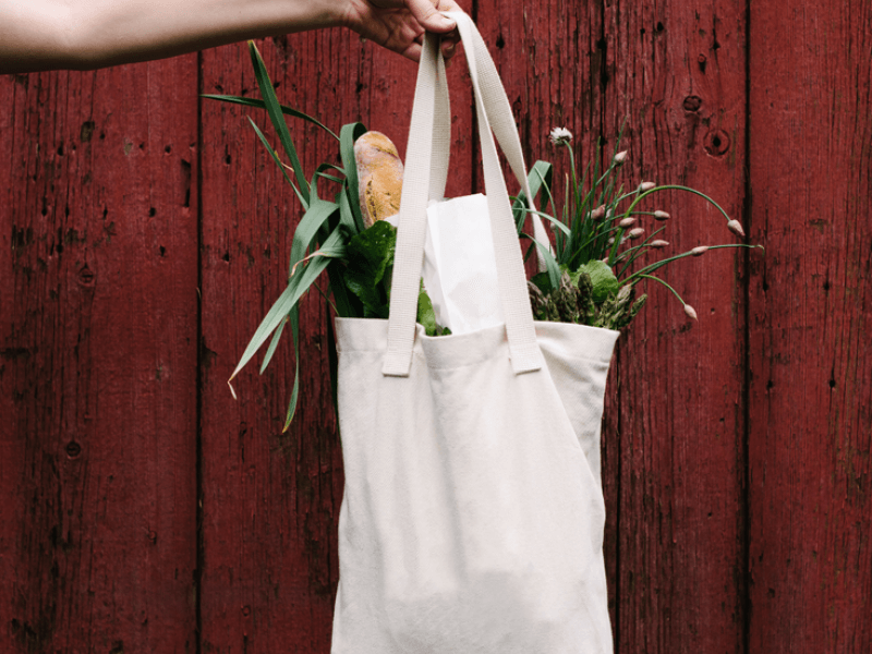 A hand holding a bag full of flowers of bread, in front of a red fence