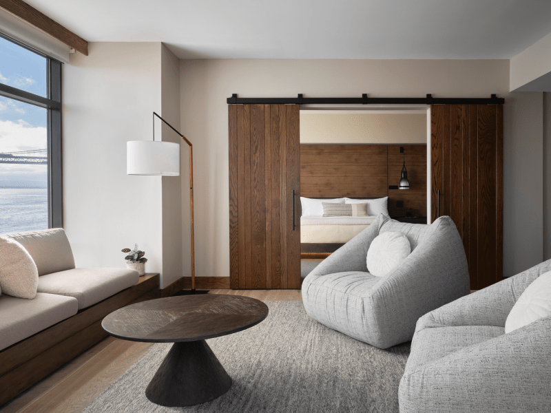 Two large gray chairs and a sofa positioned around a dark brown circular coffee table, overlooking views of the water