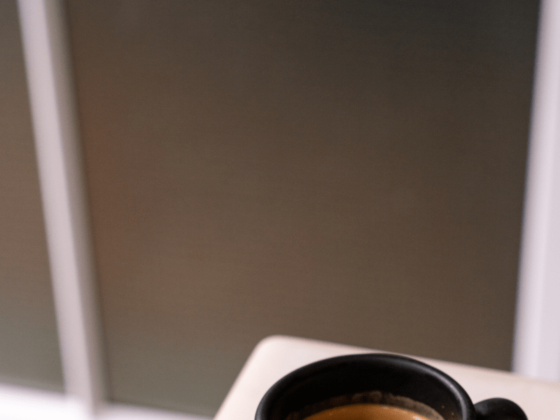 A cup of coffee in a black mug sits atop a white countertop