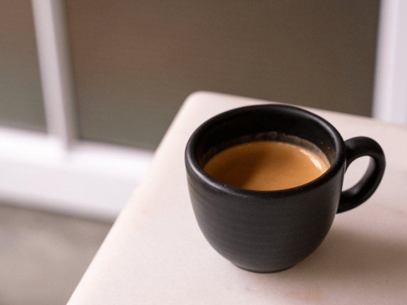 A cup of coffee in a black mug sits atop a white countertop
