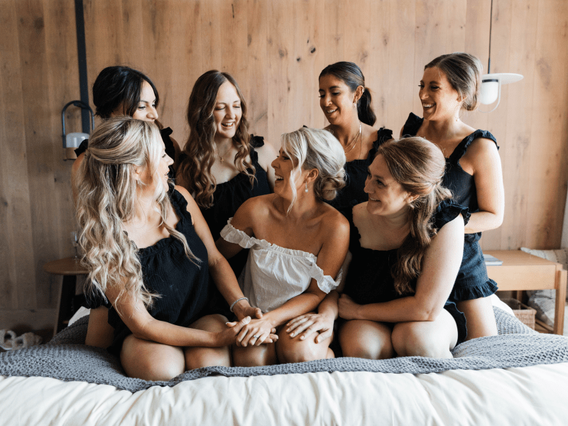 a bride surrounded by her bridal party while sitting on a bed