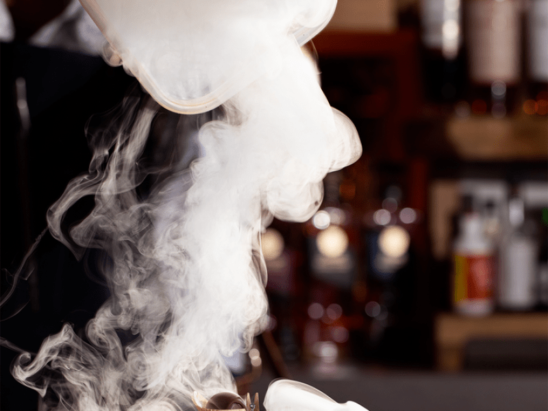 Person pouring white smoke over a drink