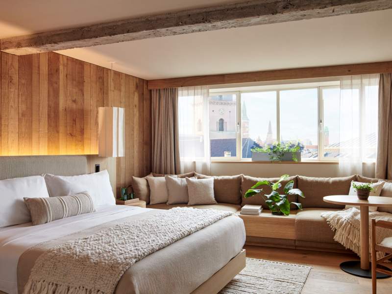 A bed in a wood-panelled room next to a window alcove bench