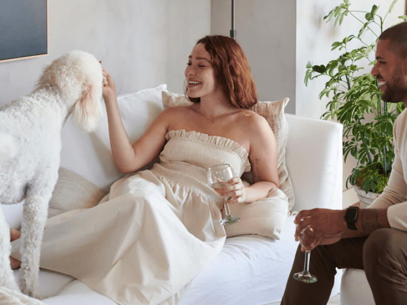 Two people sitting on couches with a drink petting a dog