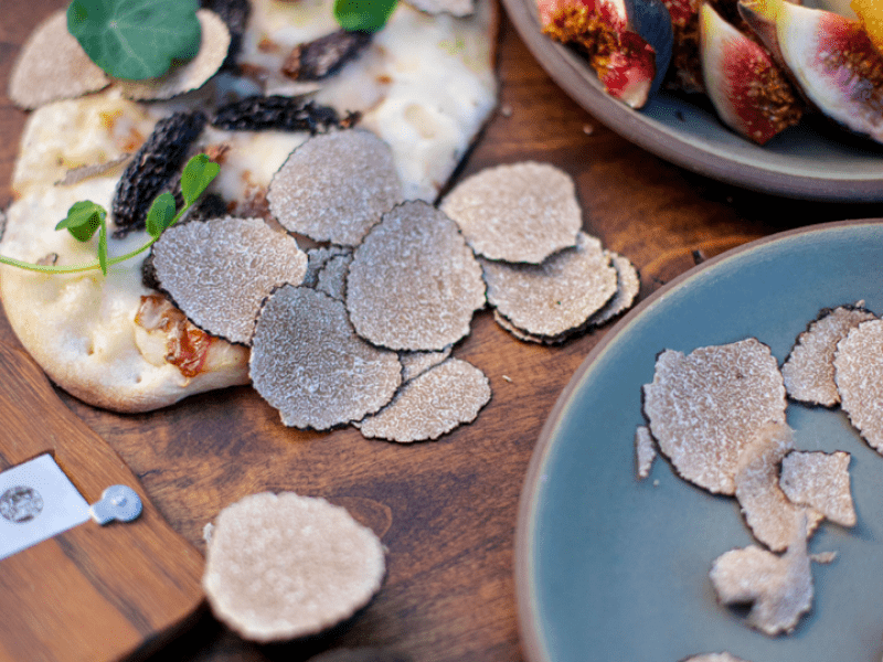 Flatbread with shaved truffle coming out of pizza oven