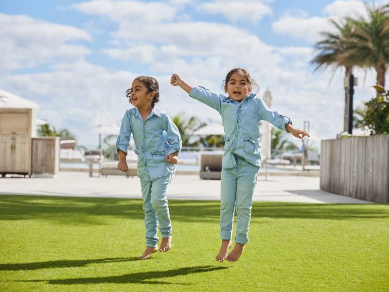 Two small children in matching denim outfits jumping and smiling for the camera