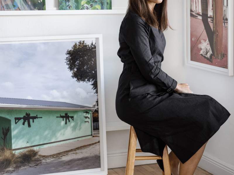 Artist sitting on stool with paintings behind here
