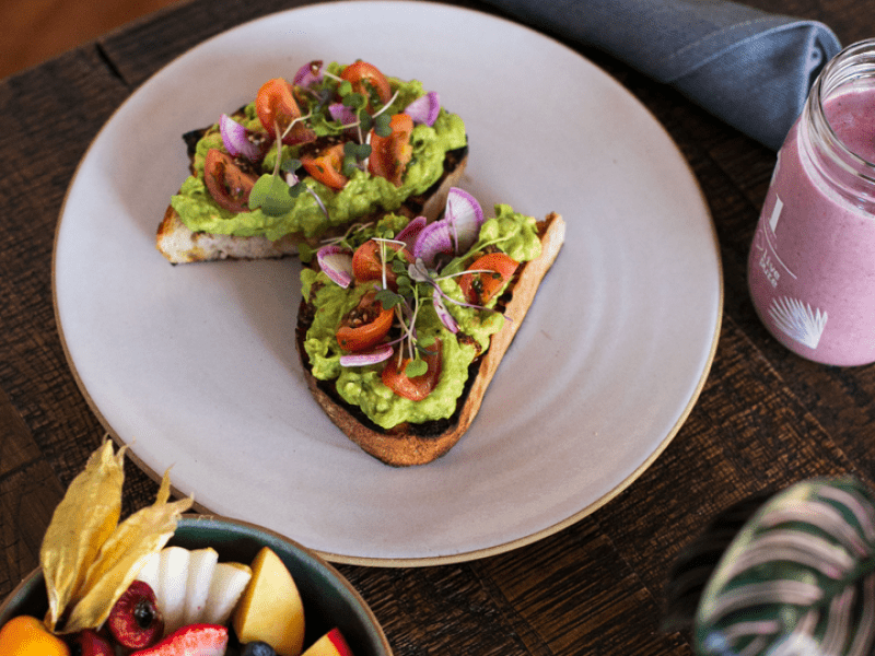 Avocado toast sandwich with a bowl of fruit and a smoothie