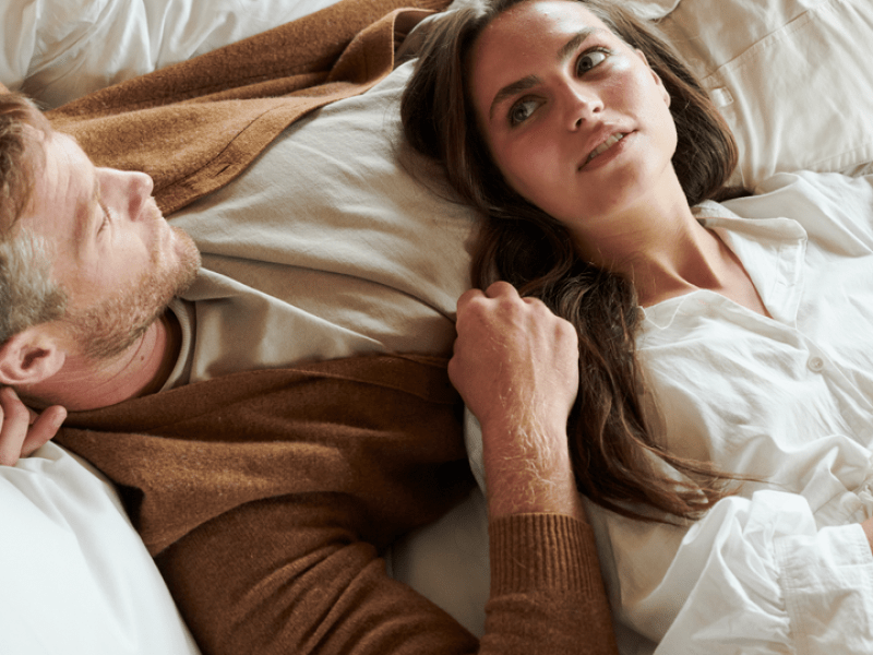 A couple, one woman with her head laying on a man, rest together in a 1 Hotels bed