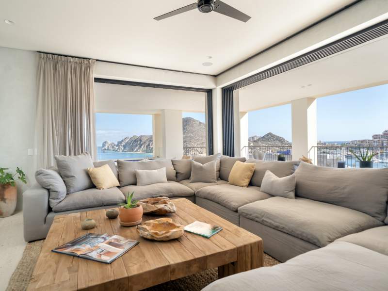 Windows with a panoramic view of the seascape outside line a large room with a wrap around sectional