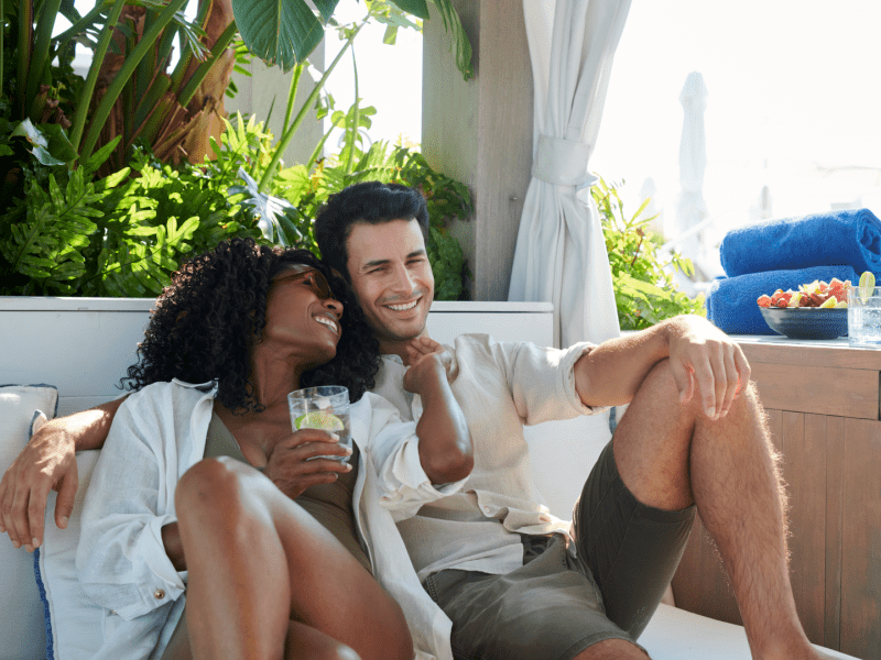 A couple sits on lounge chairs with their cocktails smiling at each other