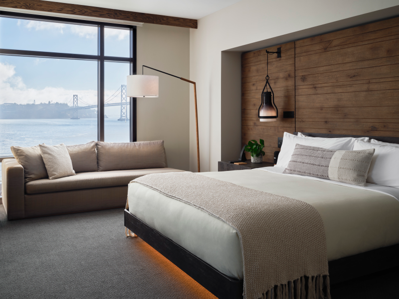 A king size bed sits center of the room, while a sofa sits positioned against a window overlooking the water