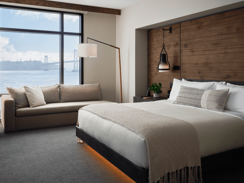A king size bed sits center of the room, while a sofa sits positioned against a window overlooking the water