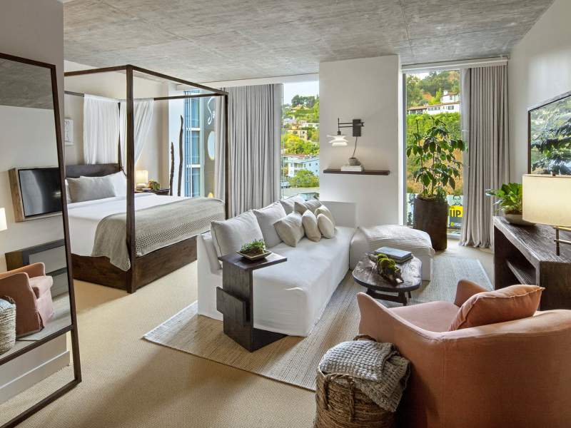 Un lit king size est placé sous un cadre à baldaquin.  Un canapé blanc est placé devant le lit, face à un téléviseur.