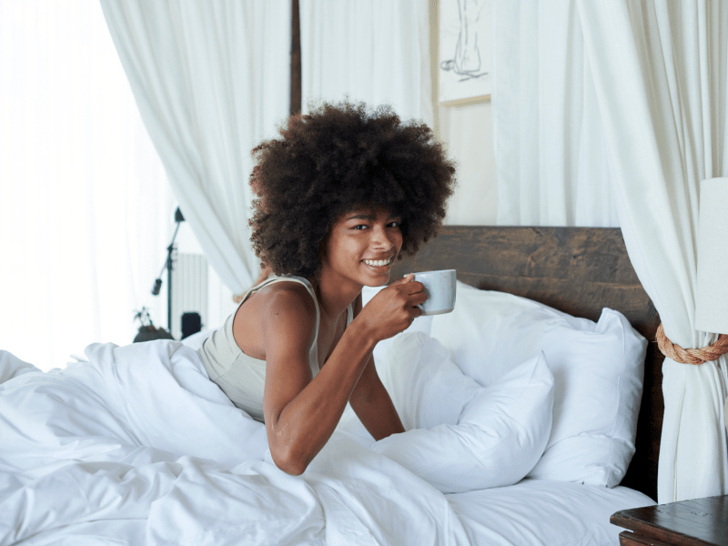 Person laying in bed drinking a cup of coffee