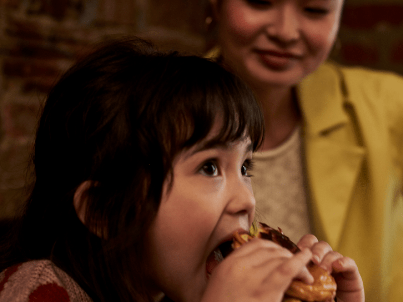 Child eating a burger with their mother watching