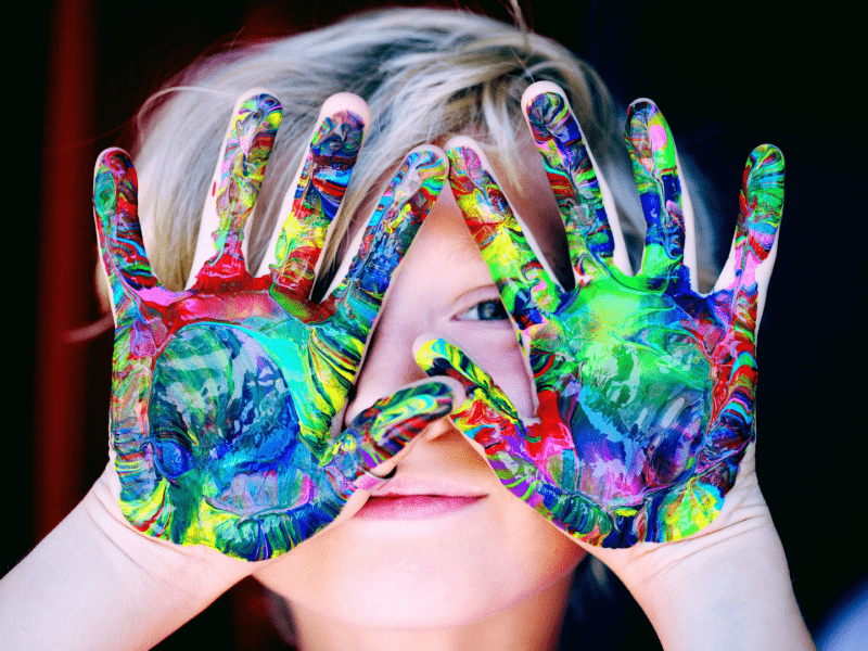 A child with painted hands covering their face