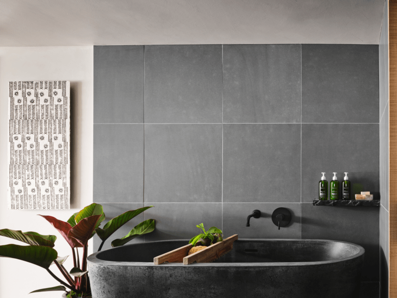 A large granite bathtub sits atop another slate of granite with a gray tile backdrop