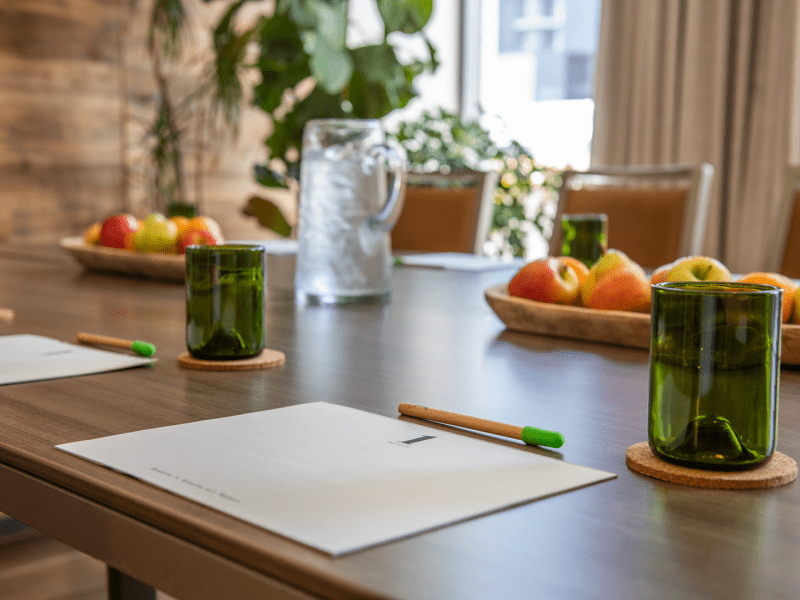 A wooden table set with offerings of fruit, drinking cups, and paper with pencil per seating arrangement