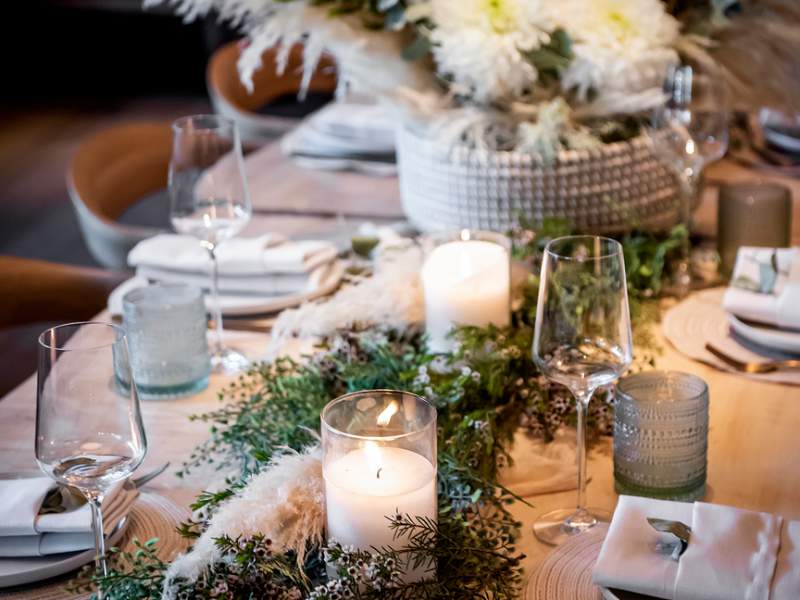 Un tavolo da banchetto in stile ligneo decorato con fiori bianchi e verdi, luci e un'elegante tavola imbandita.