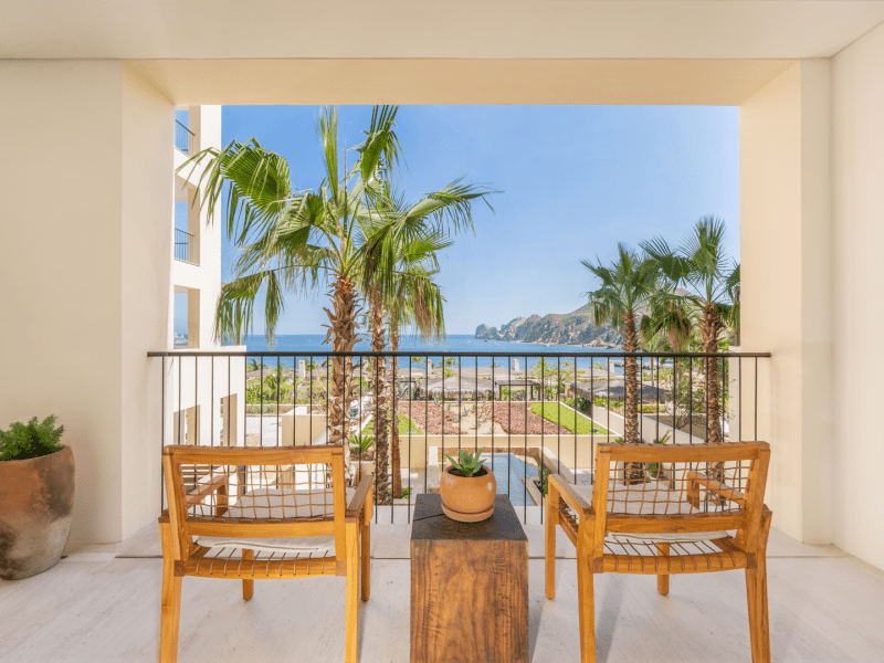 Two wooden patio chairs face outwards on the patio overlooking the beach and sea