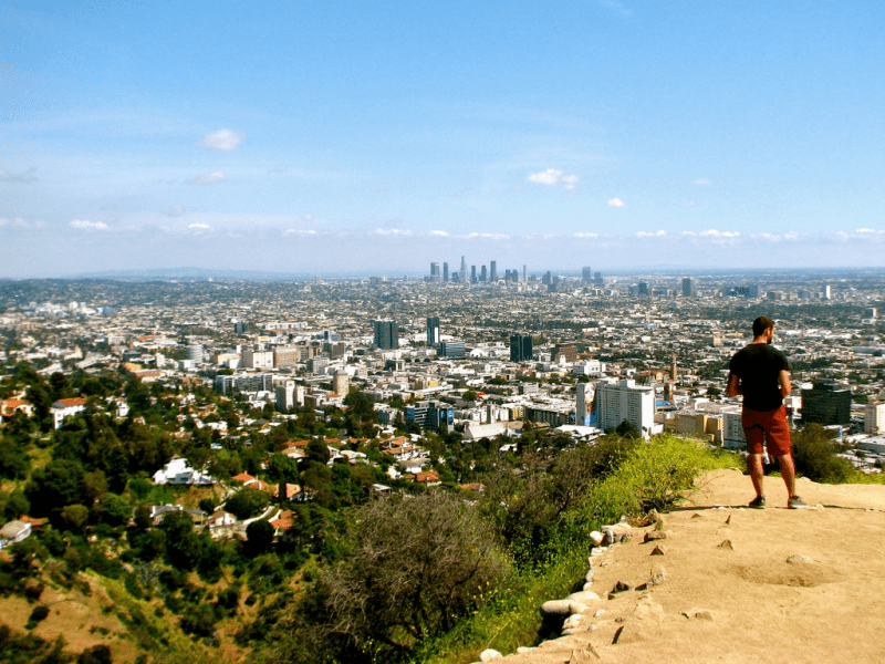 A man in athleisure stands overlooking the canyon, nearest, and city scape, further in the distance