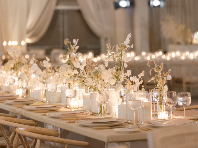 A beautifully set banquet table adorned with white flowers and glowing candles, creating a warm and elegant ambiance in a softly lit room