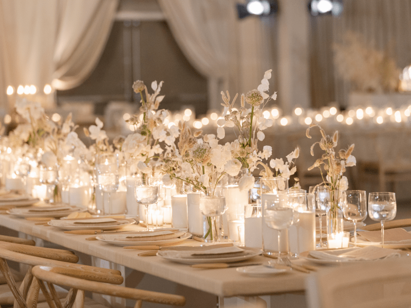 A beautifully set banquet table adorned with white flowers and glowing candles, creating a warm and elegant ambiance in a softly lit room