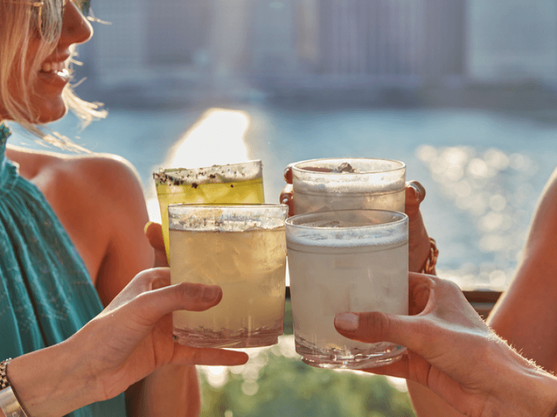 Four individuals clink their glasses together in cheers atop Harriet's rooftop bar.  Views of the city skyline visible behind them.