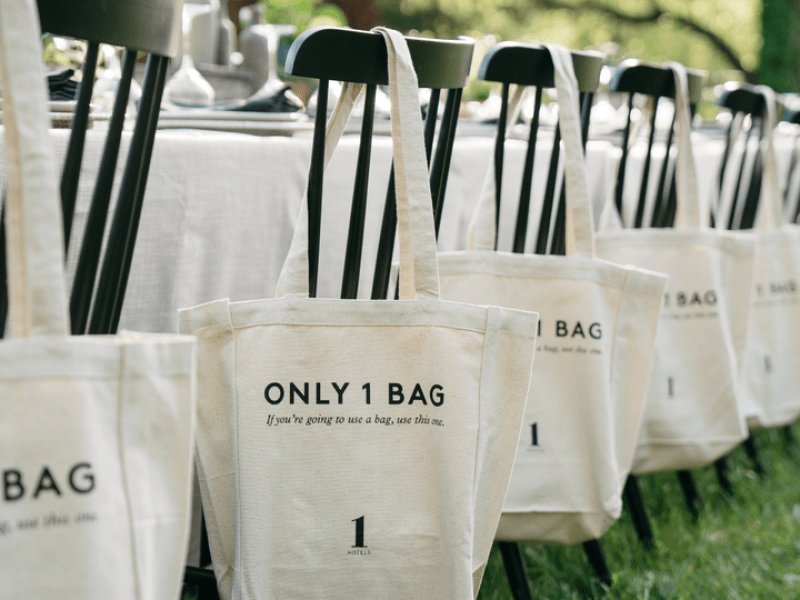 a row of chairs at a table, with tote bags hanging on them