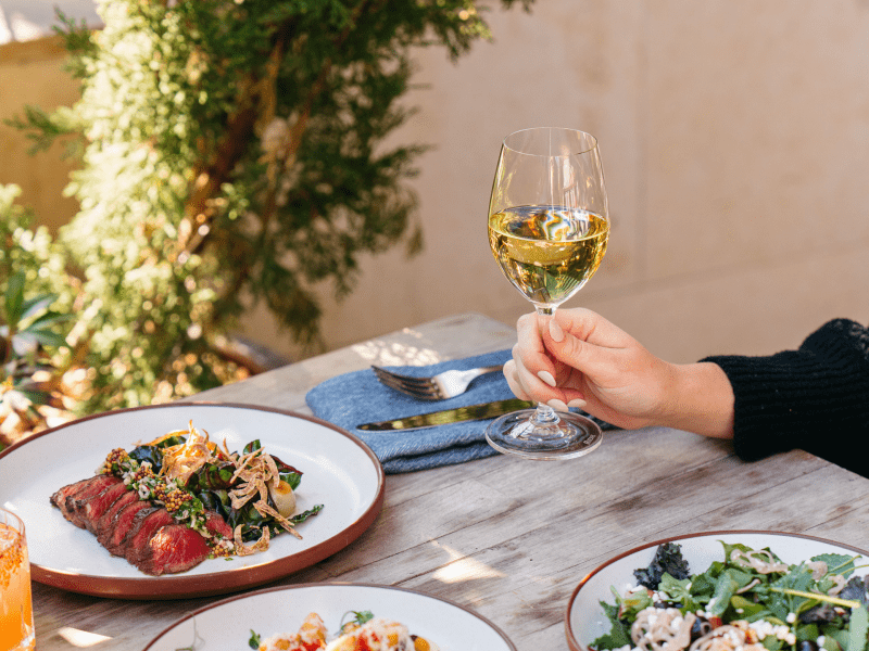 hand holding a glass of wine outside with food