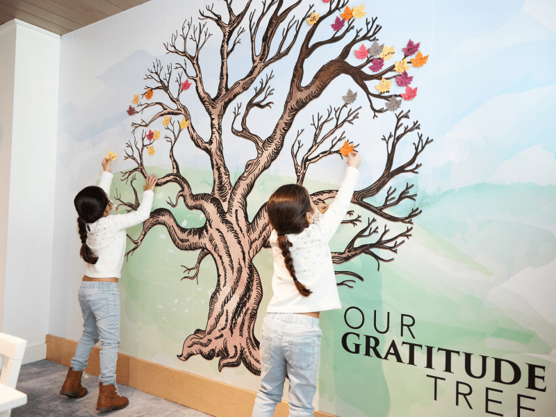 Two children putting leaves on a tree painting