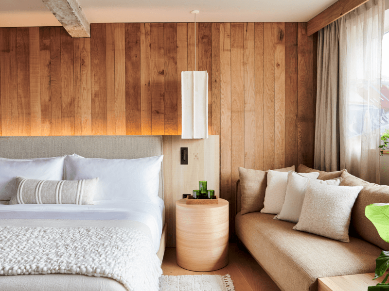 A bed in a wood-panelled room next to a window alcove bench