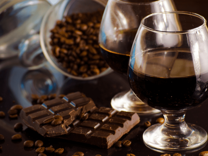 A glass of rum, a broken chocolate bar and cacao beans