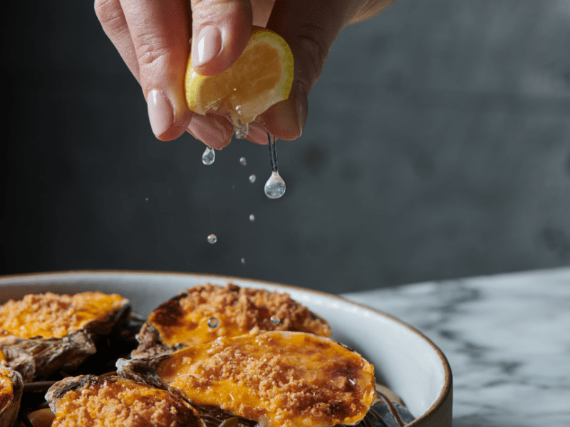 A hand squeezing a lemon onto baked oysters