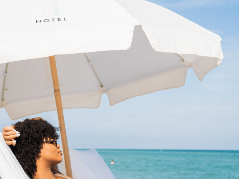 A person laying on a beach chair with a drink in their hand, under an umbrella